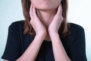 A woman touching her neck near her thyroids as if uncomfortable